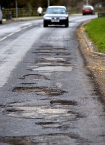 A car approaches potholes in Priory Road, Hull, East Yorkshire, UK.